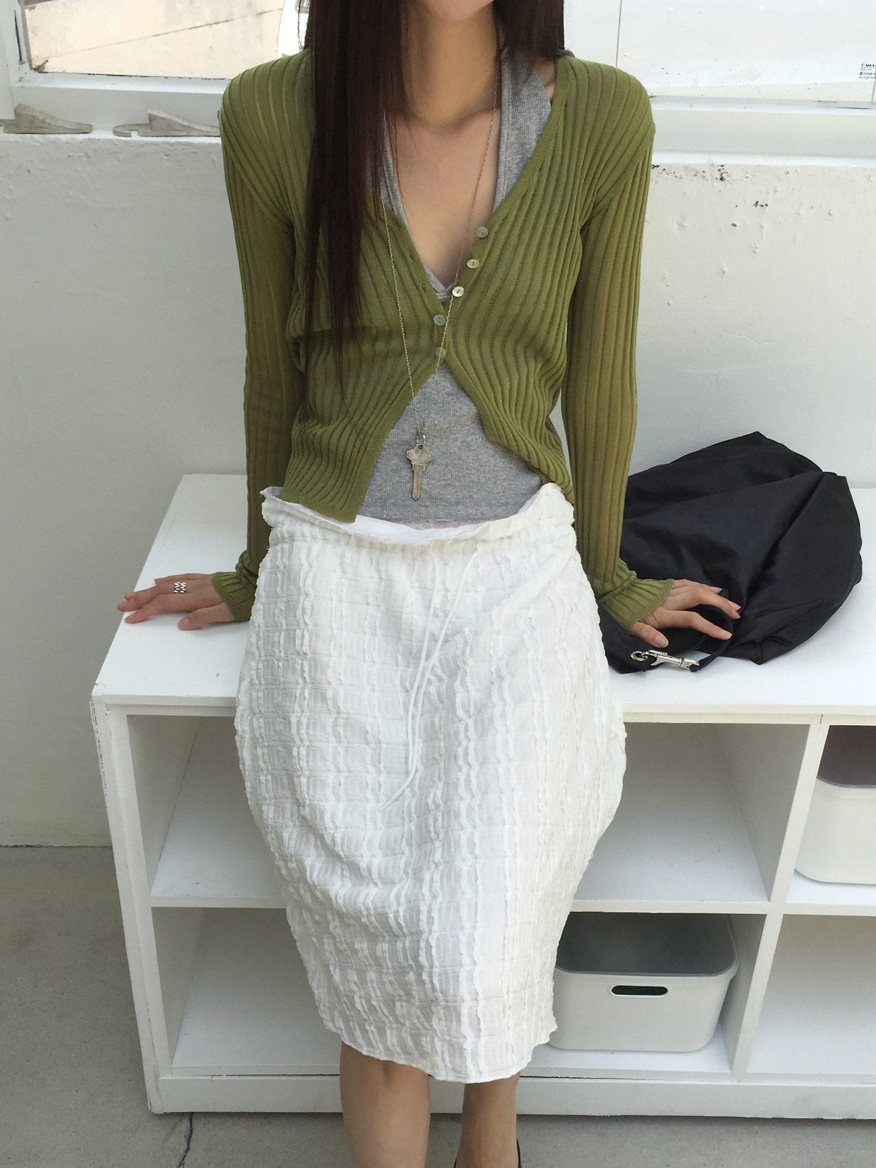 Nweol ribbed open knit crop cardigan in Olive, styled on model front view with grey tank top and white textured skirt