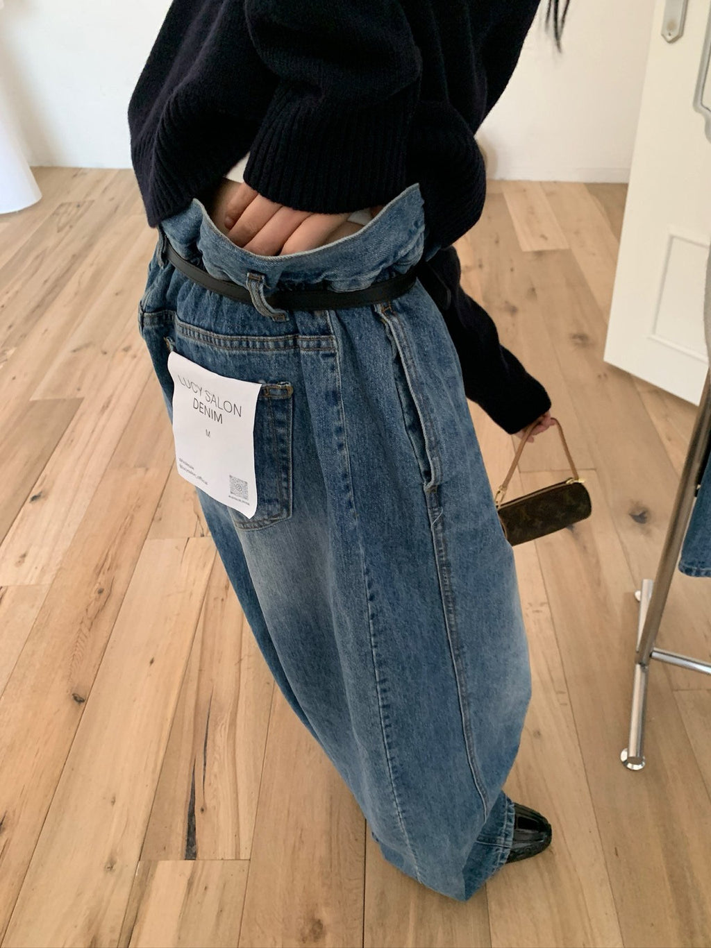 Blue pleated wide-leg jeans with black belt displayed on a hanger