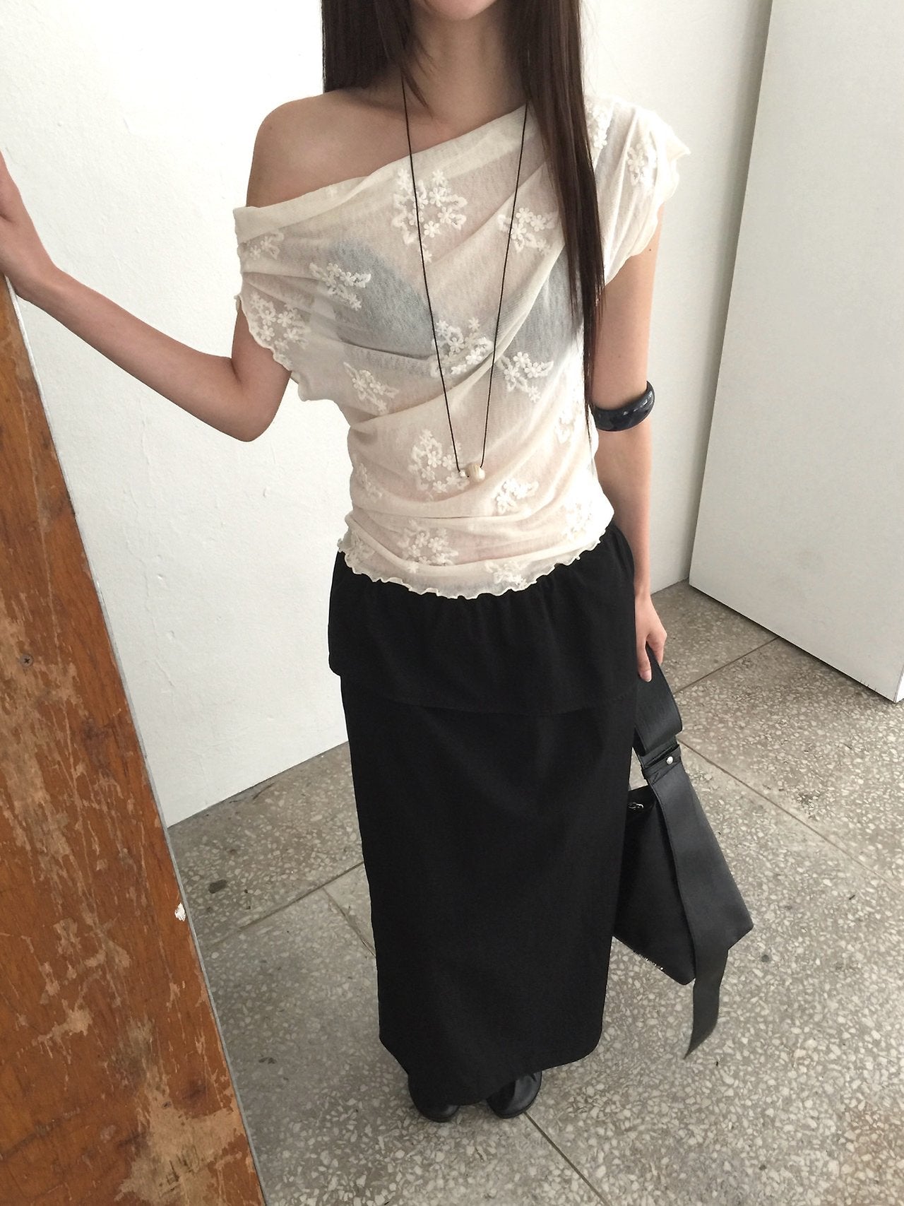 Nweol one-shoulder floral lace mesh top in Black, styled on model front view with charcoal skirt standing against wall