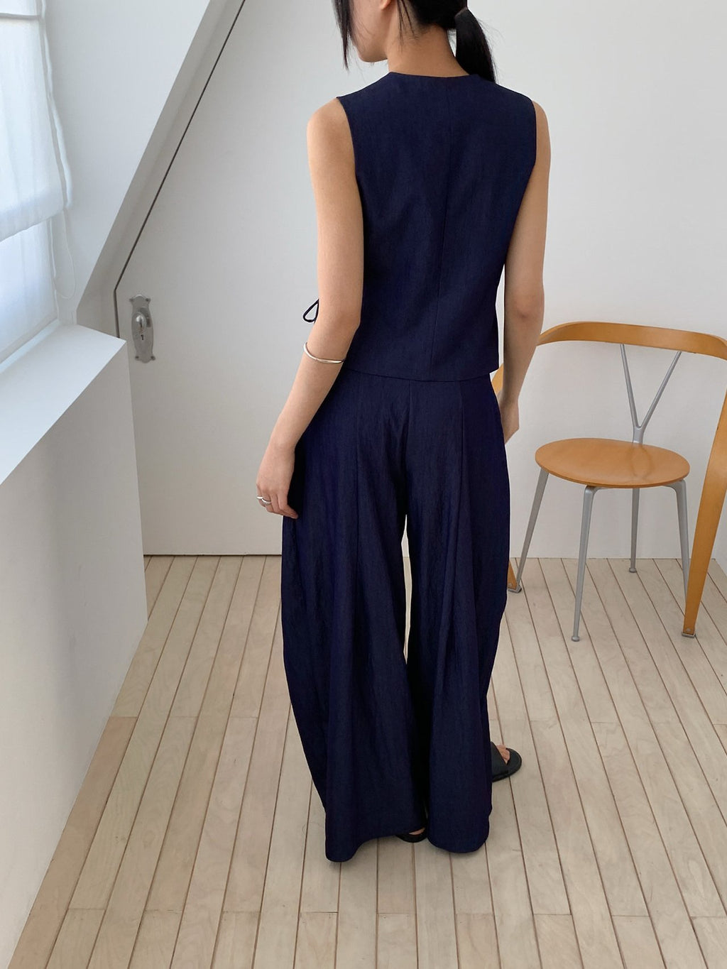 Vivel cross wrap vest in Navy, styled on model front view with navy wide leg pants seated by chair