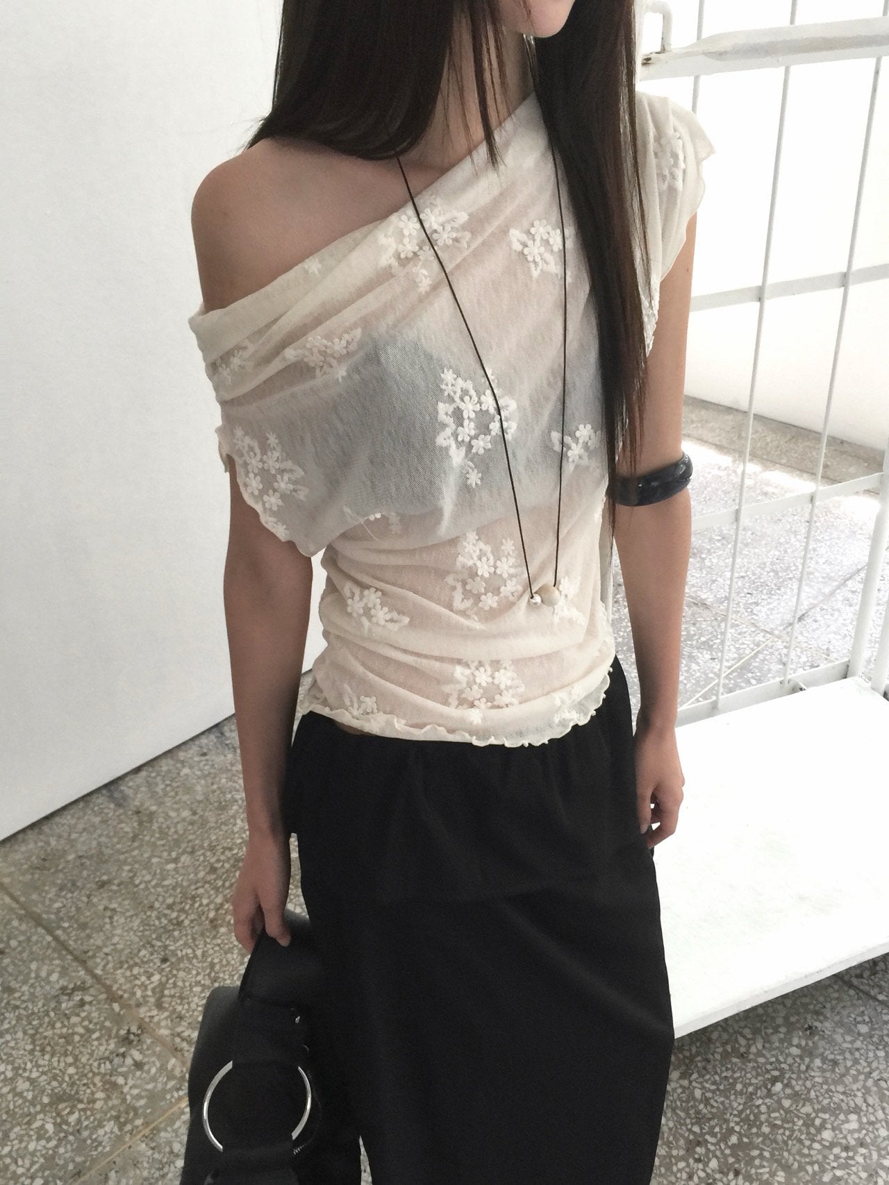 Nweol one-shoulder floral lace mesh top in Black, styled on model front view with charcoal skirt against curtain