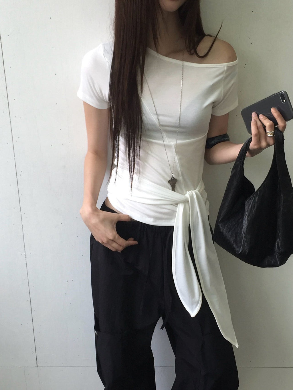 Nweol off-shoulder crop top with tie waist in Light Grey, styled on model seated front view with black maxi skirt