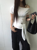 Nweol off-shoulder crop top with tie waist in Light Grey, styled on model seated front view with black maxi skirt