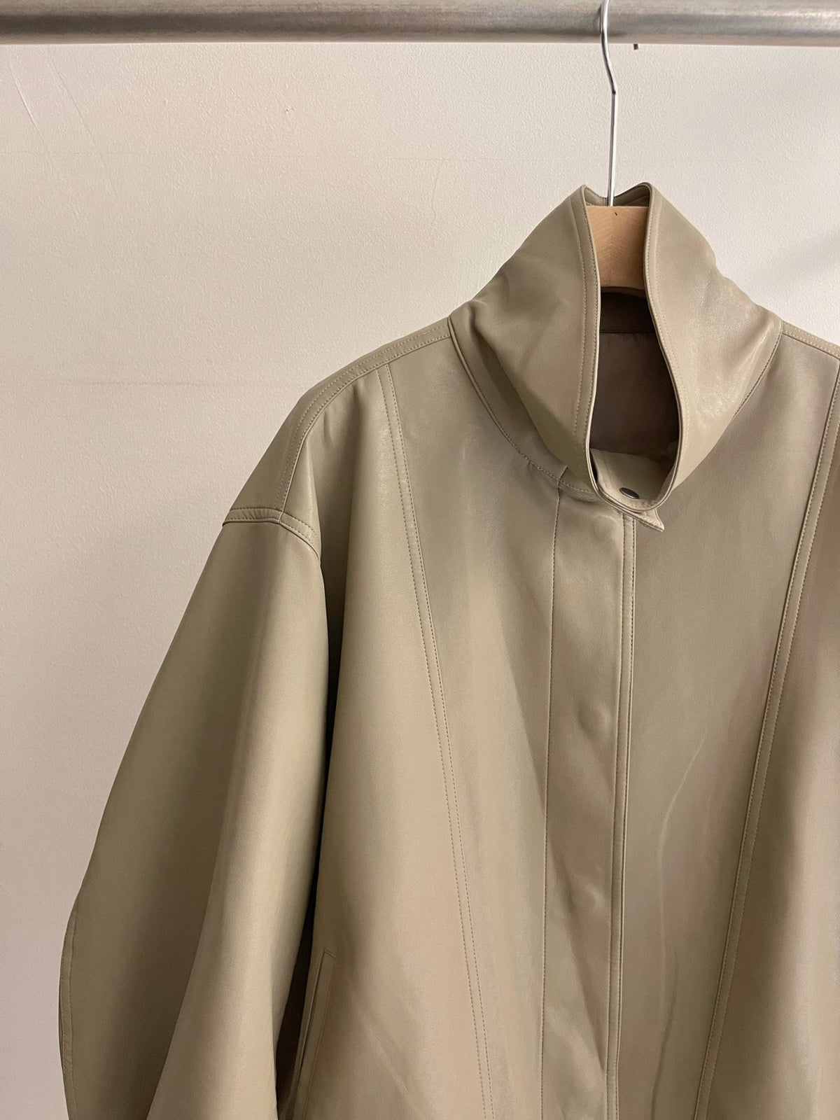 Front view of beige high-neck snap-front jacket worn with white trousers