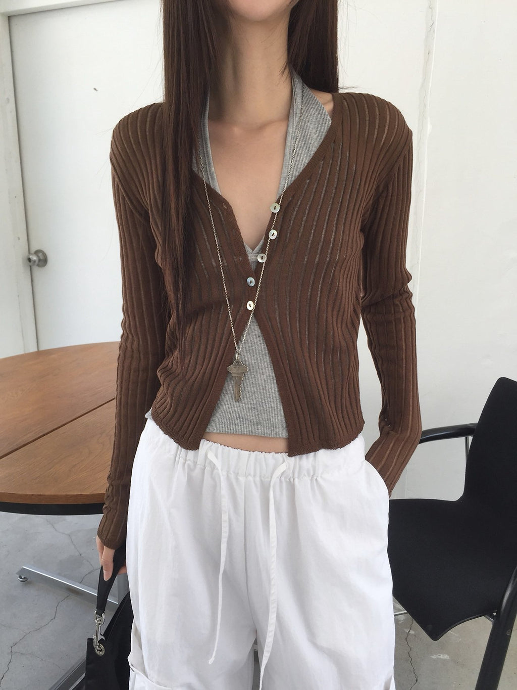 Nweol ribbed open knit crop cardigan in Olive, styled on model seated side view with white textured skirt