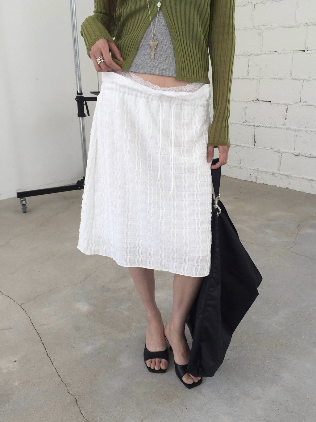 Nweol bubble texture midi skirt in Black, styled on model seated front view with white tank top and light green cardigan