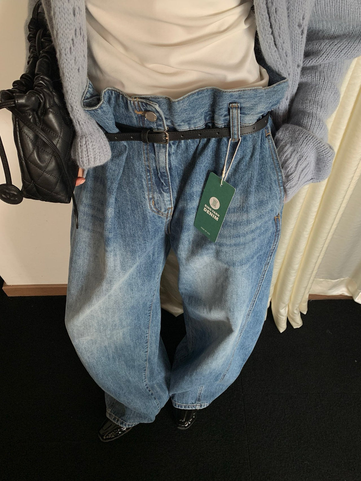 Close front view of blue pleated jeans with included black belt